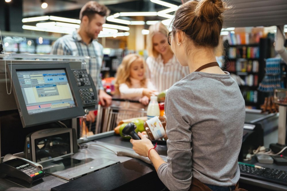 Uma atendente de caixa de um supermercado está registrando os produtos do carrinho de compras de uma família com 3 pessoas.